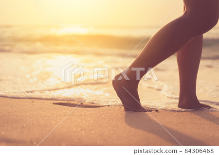 Close up woman legs walking on tropical sunset beach with smooth wave and bokeh sun light wave abstract background. Travel vacation and freedom feel good concept. 84306468
