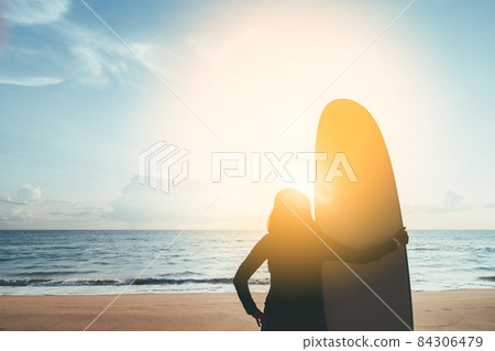 Woman hold surfboard standing at tropical sunset beach background. Summer vacation and sport adventrue concept. Woman hold surfboard standing at tropical sunset beach background. Summer vacation and sport adventrue concept. 84306479