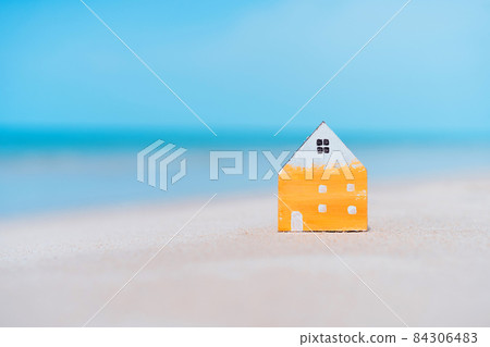 Small home model on sand beach with blue sky background. Small home model on sand beach with blue sky background. 84306483