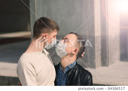 Young gay couple wearing medical mask, hugging and kissing at the city. Young gay couple wearing medical mask, hugging and kissing at the city. 84306517