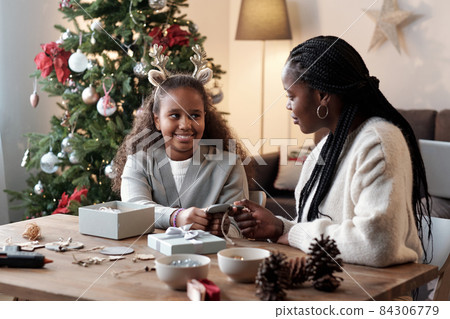 Happy little girl and her mother looking at one another while packing xmas gifts Happy little girl and her mother looking at one another while packing xmas gifts 84306779