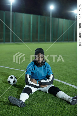 Young restful man of African ethnicity sitting on football field Young restful man of African ethnicity sitting on football field 84306970