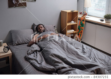 Young African man lying under grey blanket while sleeping Young African man lying under grey blanket while sleeping 84307231
