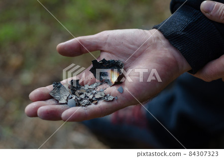 A burnt chicken egg in the hands of a man. 84307323