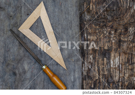 A file and a triangular ruler lie on old felt. Cracked burnt woo 84307324