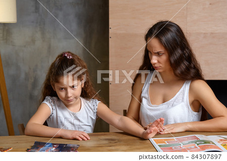 Portrait of a mother helping her small sweet and cute daughter to make her homework indoors. Happy family. Portrait of a mother helping her small sweet and cute daughter to make her homework indoors. Happy family. 84307897