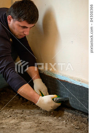 Installing waterproofing in a private home on the floor, a man attaches a waterproof tape to the bottom of the wall. 84308366
