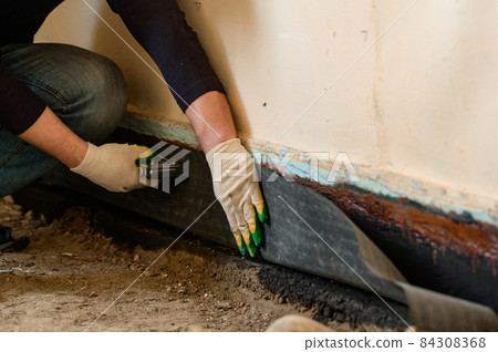 The worker attaches a bitumen tape with a stapler to protect the wood and floor from water. The worker attaches a bitumen tape with a stapler to protect the wood and floor from water. 84308368