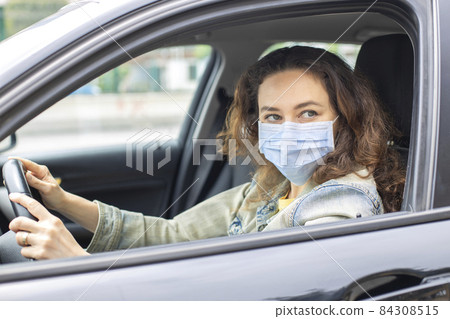 Young woman in a mask sitting in a car 84308515