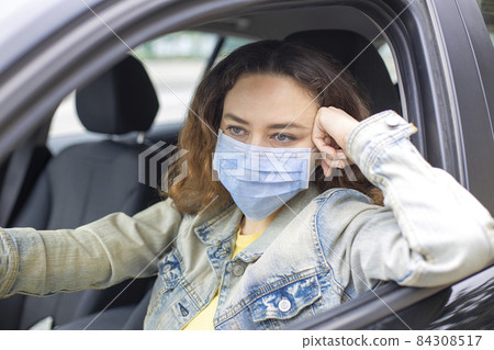 Young woman in a mask sitting in a car 84308517
