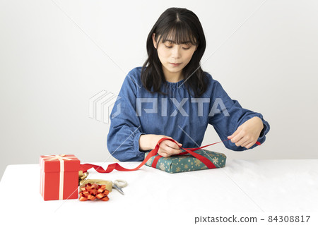 A woman hanging a red ribbon on a gift at the table 84308817