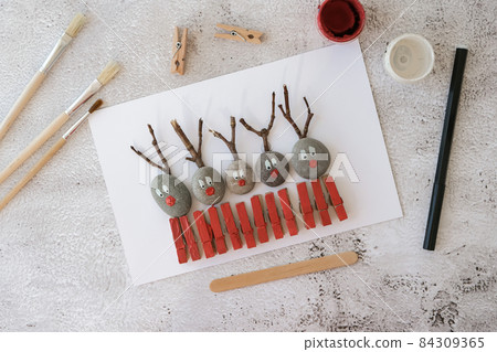 Merry Christmas deer on greeting card postcard made of pebbles, sea stones, clothespins and branches on white background. Diy Natural Eco style diy. Gift idea. Step by step. Top view. 84309365