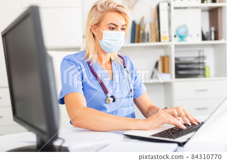 Female doctor in in protective medical mask working on laptop 84310770