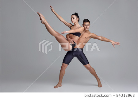 The couple of a young modern ballet dancers in black suits are posing over a gray studio background. The couple of a young modern ballet dancers in black suits are posing over a gray studio background. 84312968