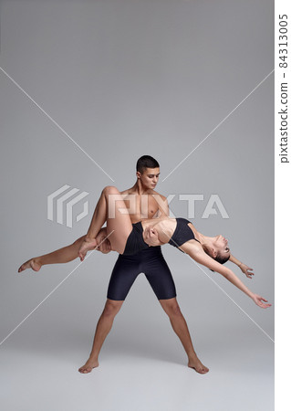The couple of a young modern ballet dancers in black suits are posing over a gray studio background. The couple of a young modern ballet dancers in black suits are posing over a gray studio background. 84313005