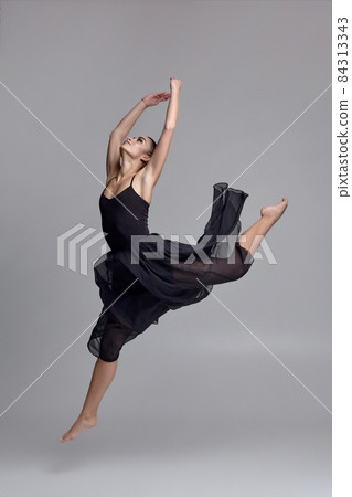 Dancing ballerina in a black dress. Contemporary graceful performance on a gray background. Dancing ballerina in a black dress. Contemporary graceful performance on a gray background. 84313343