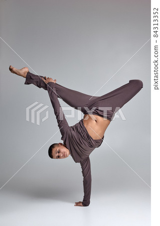 Photo of an athletic man ballet dancer dressed in a gray tracksuit, making a dance element against a gray background in studio. Photo of an athletic man ballet dancer dressed in a gray tracksuit, making a dance element against a gray background in studio. 84313352