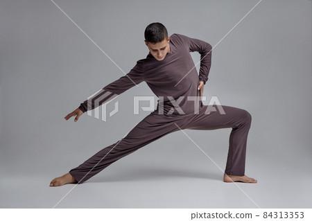 Photo of an athletic man ballet dancer dressed in a gray tracksuit, making a dance element against a gray background in studio. Photo of an athletic man ballet dancer dressed in a gray tracksuit, making a dance element against a gray background in studio. 84313353