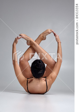 Studio photo of a beautiful woman ballerina dressed in black two-piece swimsuit doing a dance element on a gray background. Studio photo of a beautiful woman ballerina dressed in black two-piece swimsuit doing a dance element on a gray background. 84313354