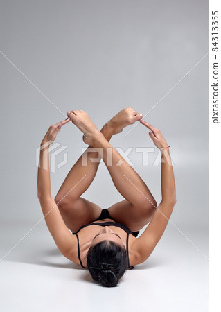 Studio photo of a beautiful woman ballerina dressed in black two-piece swimsuit doing a dance element on a gray background. Studio photo of a beautiful woman ballerina dressed in black two-piece swimsuit doing a dance element on a gray background. 84313355