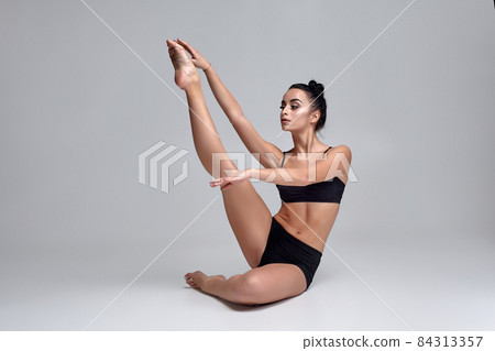 Studio photo of a beautiful woman ballerina dressed in black two-piece swimsuit doing a dance element on a gray background. Studio photo of a beautiful woman ballerina dressed in black two-piece swimsuit doing a dance element on a gray background. 84313357