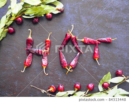 The letters are made from red hot pepper.The word hot on a dark background with a bay leaf around the edge. The letters are made from red hot pepper.The word hot on a dark background with a bay leaf around the edge. 84313448