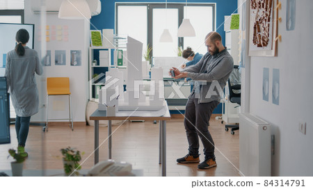 Architect using mobile phone to create blueprints plan with building model and maquette Architect using mobile phone to create blueprints plan with building model and maquette 84314791