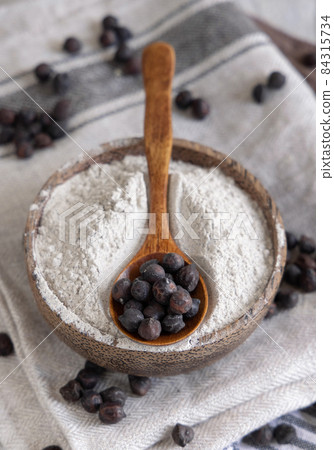 Bowl of black chickpea flour and beans with a wooden spoon closeup Bowl of black chickpea flour and beans with a wooden spoon closeup 84315734