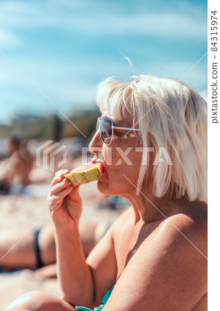 Adult blond caucasian woman in sunglasses eating big piece of watermelon Adult blond caucasian woman in sunglasses eating big piece of watermelon 84315974