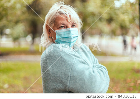 Blonde woman wearing protective face mask and in a warm cashmere scarf in park outdoor during quarantine of coronavirus pandemic. Copy, empty space for text Blonde woman wearing protective face mask and in a warm cashmere scarf in park outdoor during quarantine of coronavirus pandemic. Copy, empty space for text 84316115