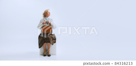 Portrait of senior sad woman in retro style, fashion of 70s, 60s years sitting in chair isolated on white studio background with copyspace for ad. Portrait of senior sad woman in retro style, fashion of 70s, 60s years sitting in chair isolated on white studio background with copyspace for ad. 84316213