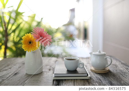 White coffee cup and tea pot with notebook and gerbera flowers 84316575