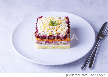 Herring salad under a fur coat. Traditional Russian multilayered salad from herring, beets, potatoes, carrots and eggs. Close-up, grey background. Herring salad under a fur coat. Traditional Russian multilayered salad from herring, beets, potatoes, carrots and eggs. Close-up, grey background. 84317274