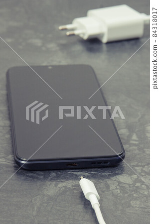 Black smartphone and unconnected cable of charger. Telephone charging Black smartphone and unconnected cable of charger. Telephone charging 84318017