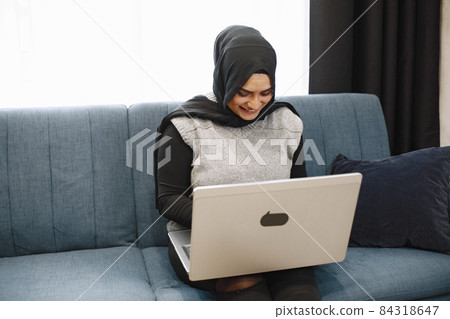 Arabic woman in headscarf using laptop at home, paying for utilities online. Arabic woman in headscarf using laptop at home, paying for utilities online. 84318647