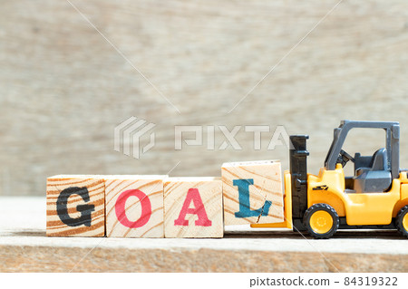 Toy forklift hold letter block l to complete word goal on wood background 84319322