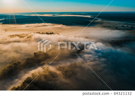 Aerial view of a beautiful summer landscape with a fog while dawn. Photo from drone of a foggy landscape in spring. Top view to land while sunrise. Early morning in nature, misty weather. Aerial view of a beautiful summer landscape with a fog while dawn. Photo from drone of a foggy landscape in spring. Top view to land while sunrise. Early morning in nature, misty weather. 84321132