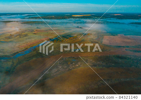 Aerial view of a beautiful summer landscape with a fog while dawn. Photo from drone of a foggy landscape in spring. Top view to land while sunrise. Early morning in nature, misty weather. Aerial view of a beautiful summer landscape with a fog while dawn. Photo from drone of a foggy landscape in spring. Top view to land while sunrise. Early morning in nature, misty weather. 84321140