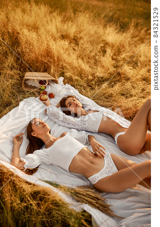Two women in lingerie lying on blanket in field Two women in lingerie lying on blanket in field 84321529