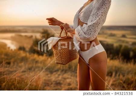 Woman in white lingerie holds basket in the field Woman in white lingerie holds basket in the field 84321538