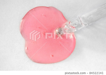 Pipette with pink fluid hyaluronic acid on white background. Cosmetics and healthcare concept. Dose of serum or retinol with air bubbles. Flatlay. Luxury gel or beauty product presentation in macro 84322141