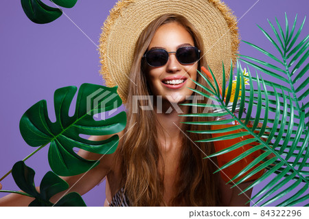 Portrait of happy girl wears in bikini, straw hat and sunglasses who stands between tropical plants Portrait of happy girl wears in bikini, straw hat and sunglasses who stands between tropical plants 84322296