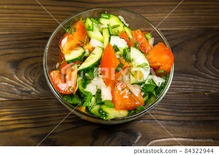 Fresh salad with tomato, cucumber, onion, parsley and dill in glass bowl on wooden table 84322944