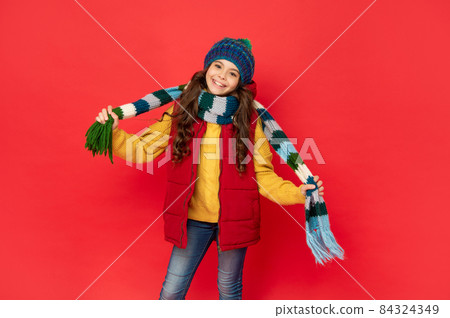 happy kid in knitted winter hat hold scarf on red background, season fashion happy kid in knitted winter hat hold scarf on red background, season fashion 84324349