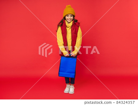 happy kid in winter hat hold shopping bags on red background, shopping 84324357
