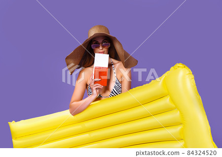 Beauty girl in sunhat going to travel stands with yellow inflatable mattress shows ticket, passport Beauty girl in sunhat going to travel stands with yellow inflatable mattress shows ticket, passport 84324520