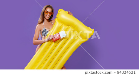 Smiling girl ready to summer vacations shows tickets with passport while holding inflatable mattress Smiling girl ready to summer vacations shows tickets with passport while holding inflatable mattress 84324521