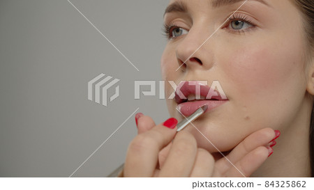 Makeup artist or stylist applies lipstick  to the lips of the female model. Visagiste making make up applying lipstick on a lip. 84325862