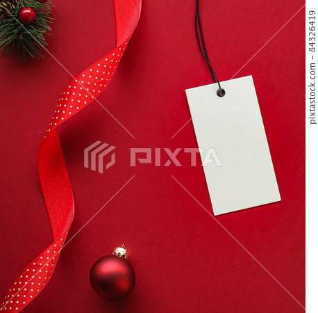 Christmas sale and holiday fashion design concept. Blank clothing tag and xmas decoration and ornaments on red paper background as flatlay mockup 84326419