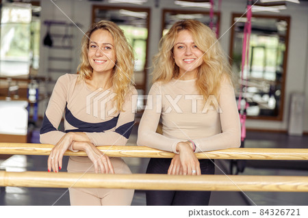 Portrait of cheerful sporty young women smiling at camera while leaning on ballet barre after exercising in modern pilates studio 84326721